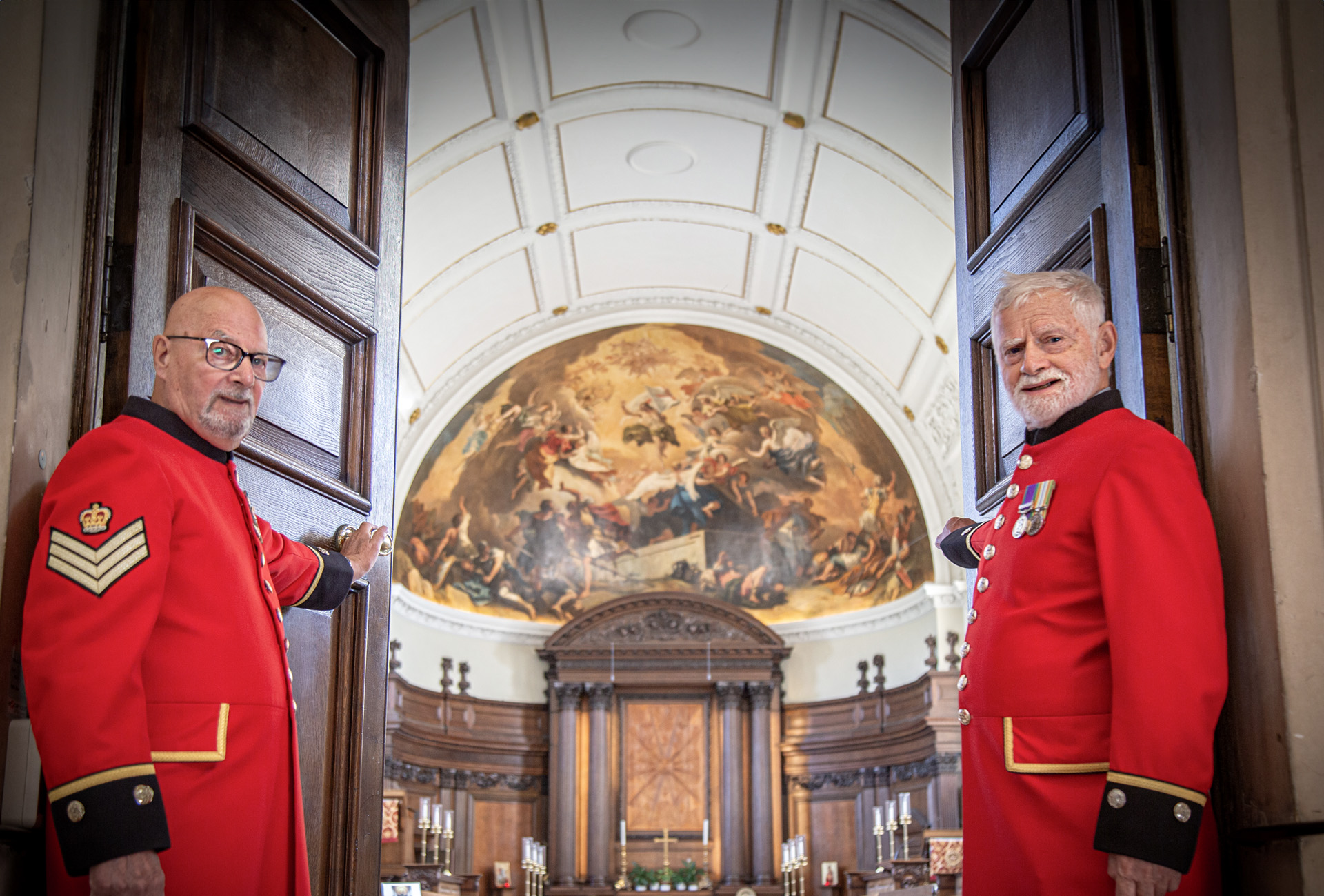 Two Chelsea Pensioners stand aside to welcome you as they open the doors of the Wren Chapel