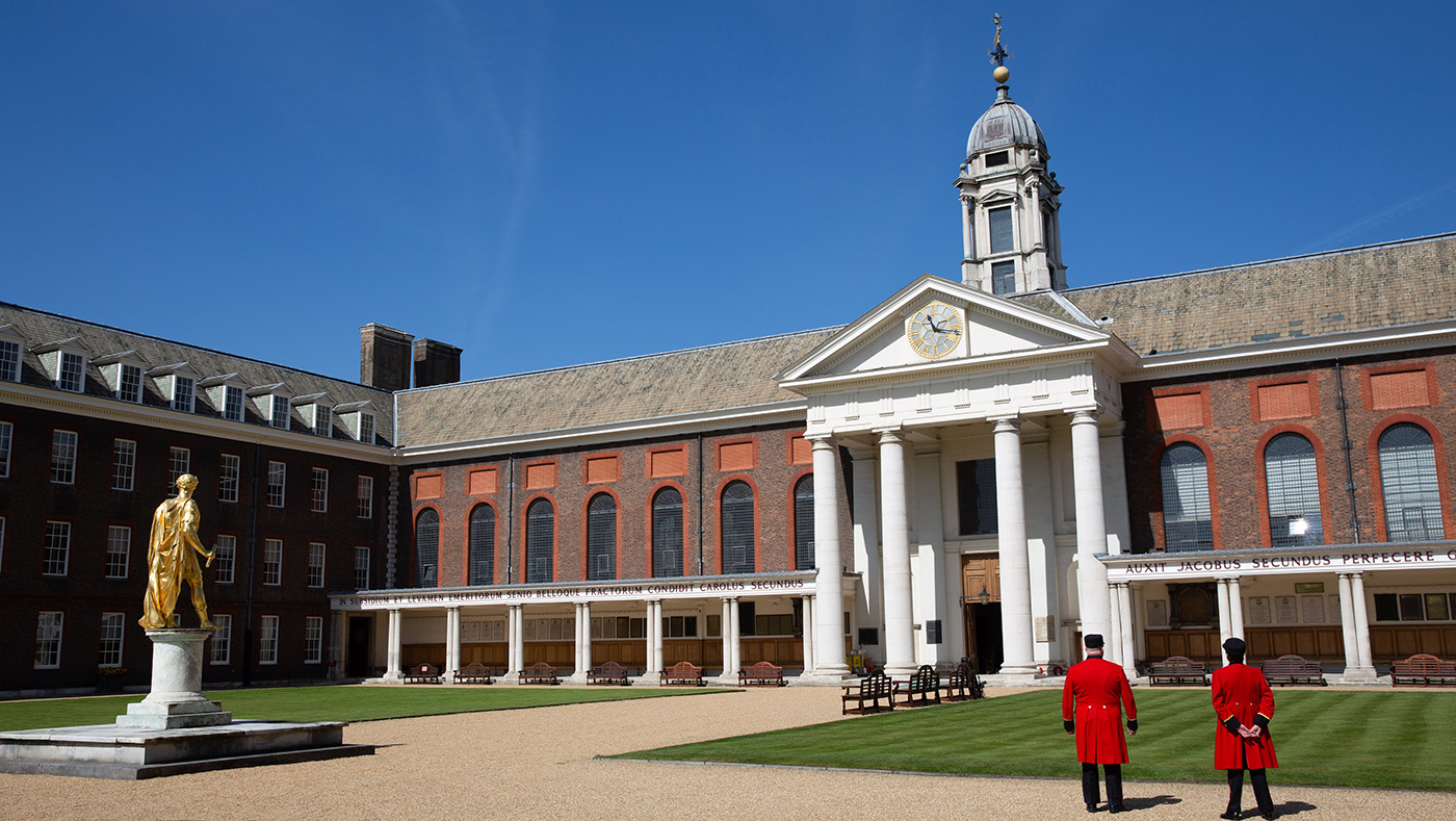 Chelsea Pensioners standing with their back to camera in Figure Court looking towards The Royal Hospital Chelsea. Gold statue of King Charles II in the distance