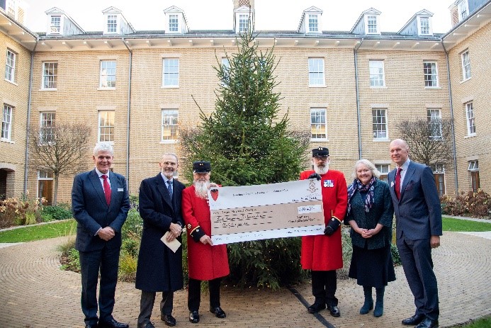 People handing large cheque to two Chelsea Pensioners dressed in red uniforms