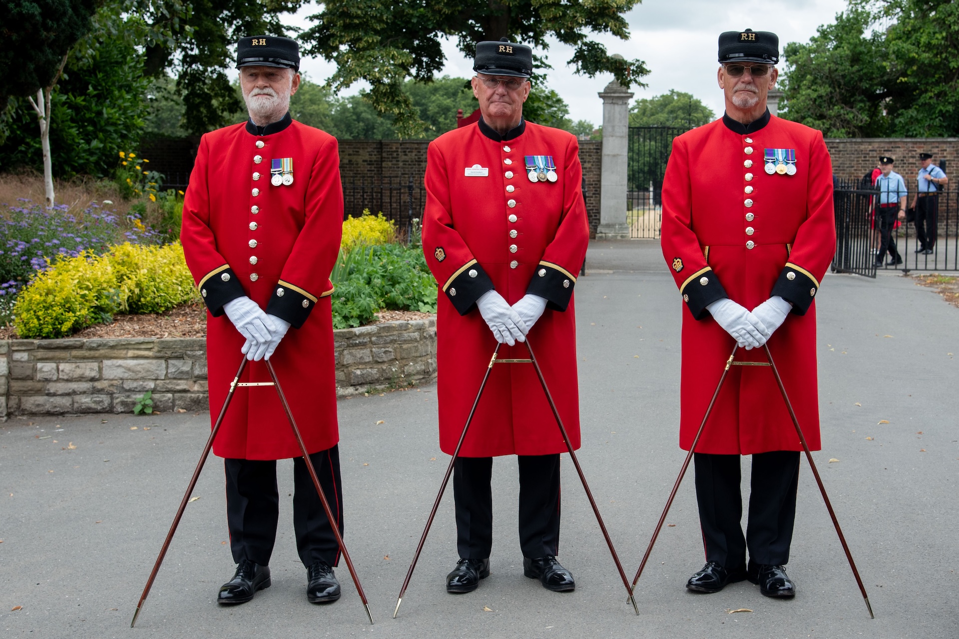 Chelsea Pensioners stand dressed in Scarlet and holding their pace sticks 