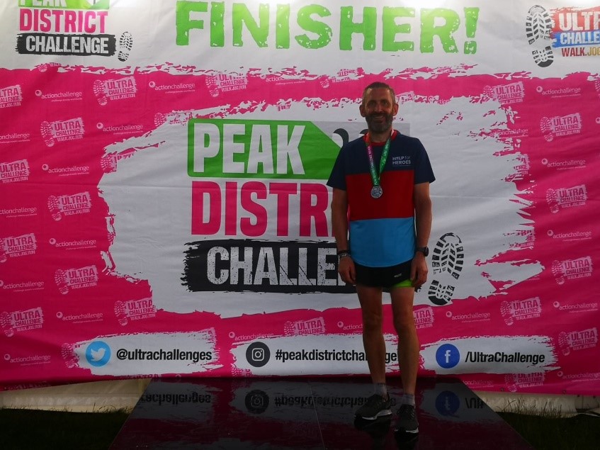 Man smiling in front of Peak District Challenge Finisher backdrop