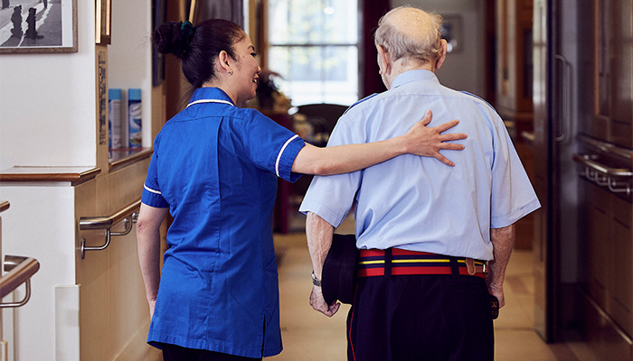 A nurse puts a hand of support on the back of a Chelsea Pensioner with a walking stick