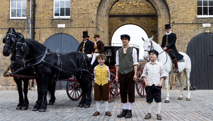 A group of historic reenactors gather alongside horses and a traditional 19th century cart in the redeveloped Soane Stable Yard at The Royal Hospital Chelsea