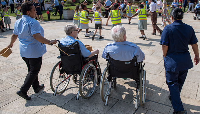 Carers pushing Chelsea Pensioners in wheelchairs at a lively outdoor event