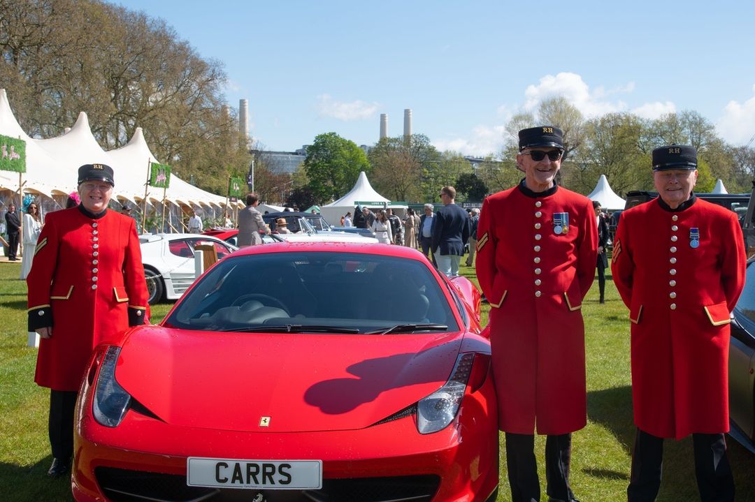 Chelsea Pensioners stand alongside a red Ferrari during the Salon Privé luxury car show