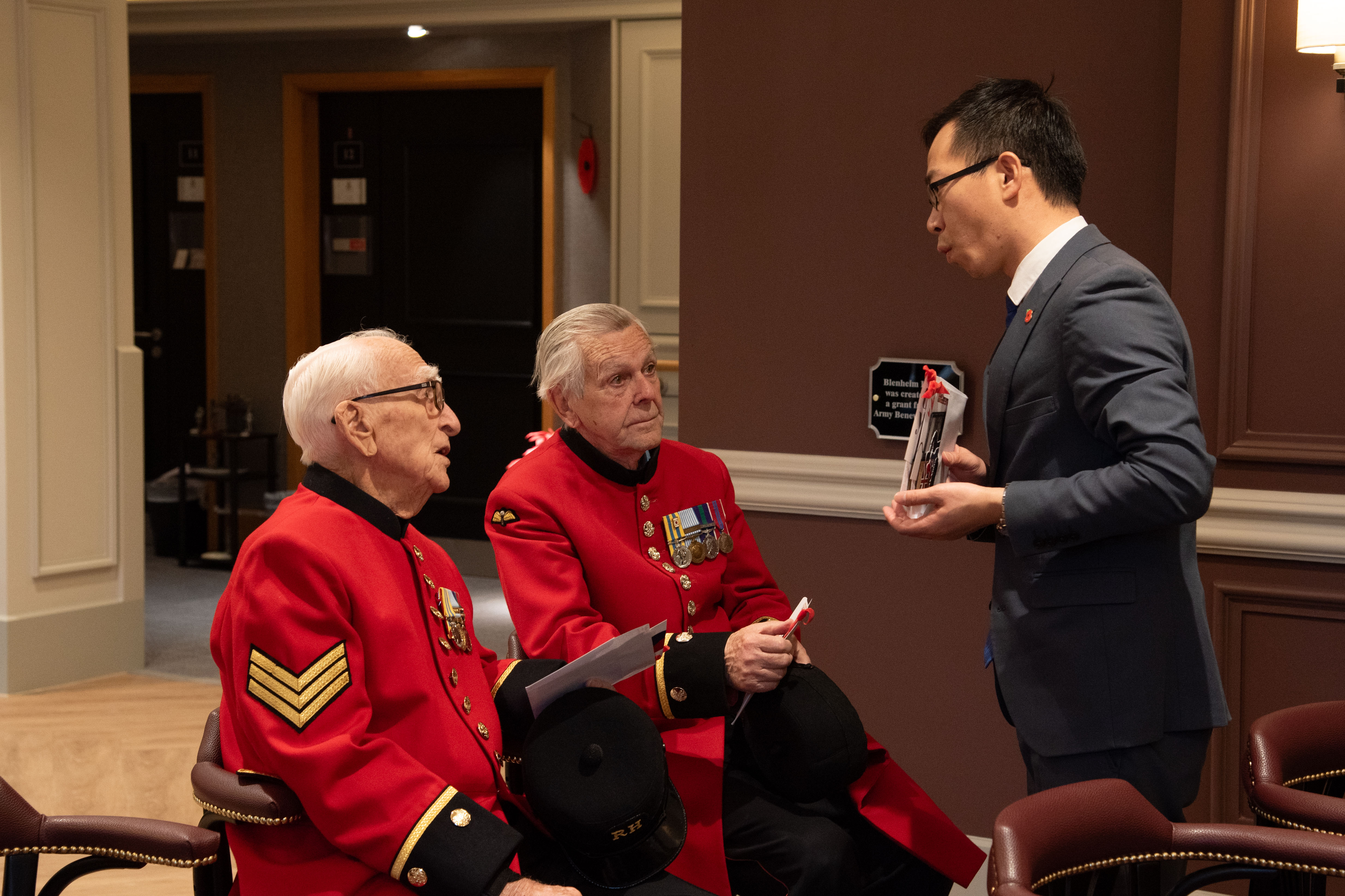 Timothy Cho presents two Chelsea Pensioners in scarlet coats with a card to thank them for their service