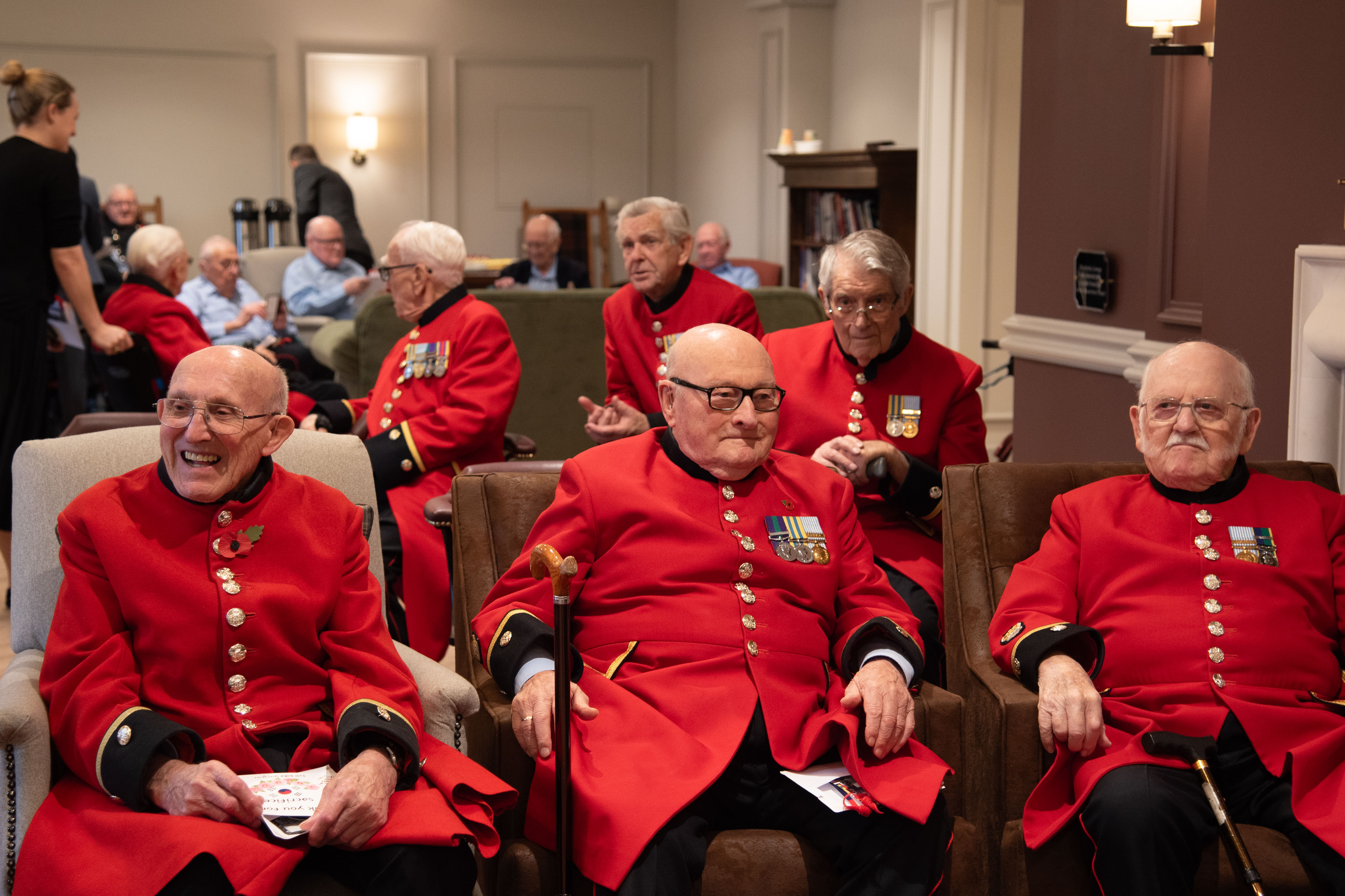 Chelsea Pensioner Korean War Veterans sit in scarlet coats smiling