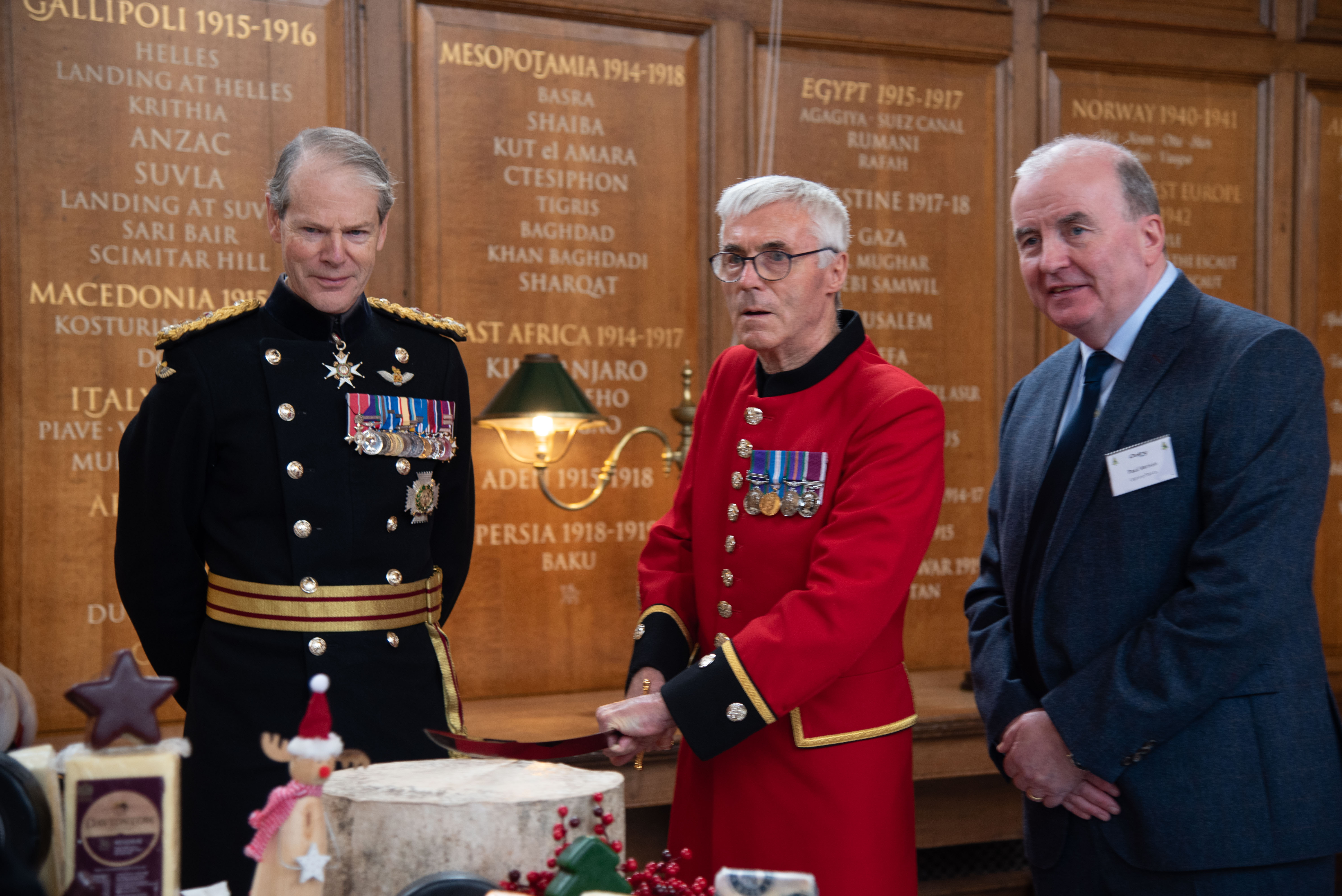 Chelsea Pensioner in scarlets cuts ceremonial cheese with a sword stood next to the Governor of the Royal Hospital and Chairman of Dairy UK