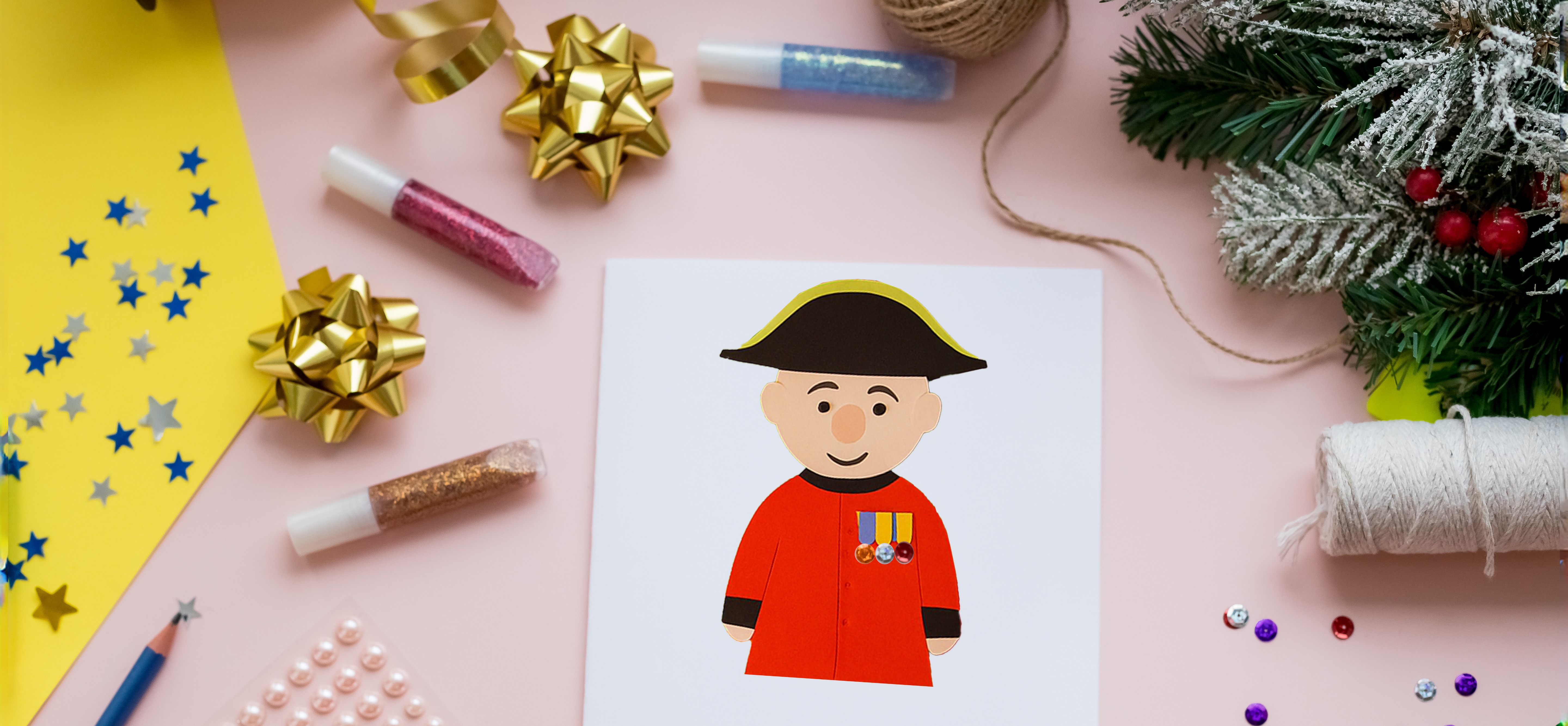 A colourful table adorned with craft making suppliers a Christmas Garlands. A Christmas card depicts a hand crafted Chelsea Pensioner