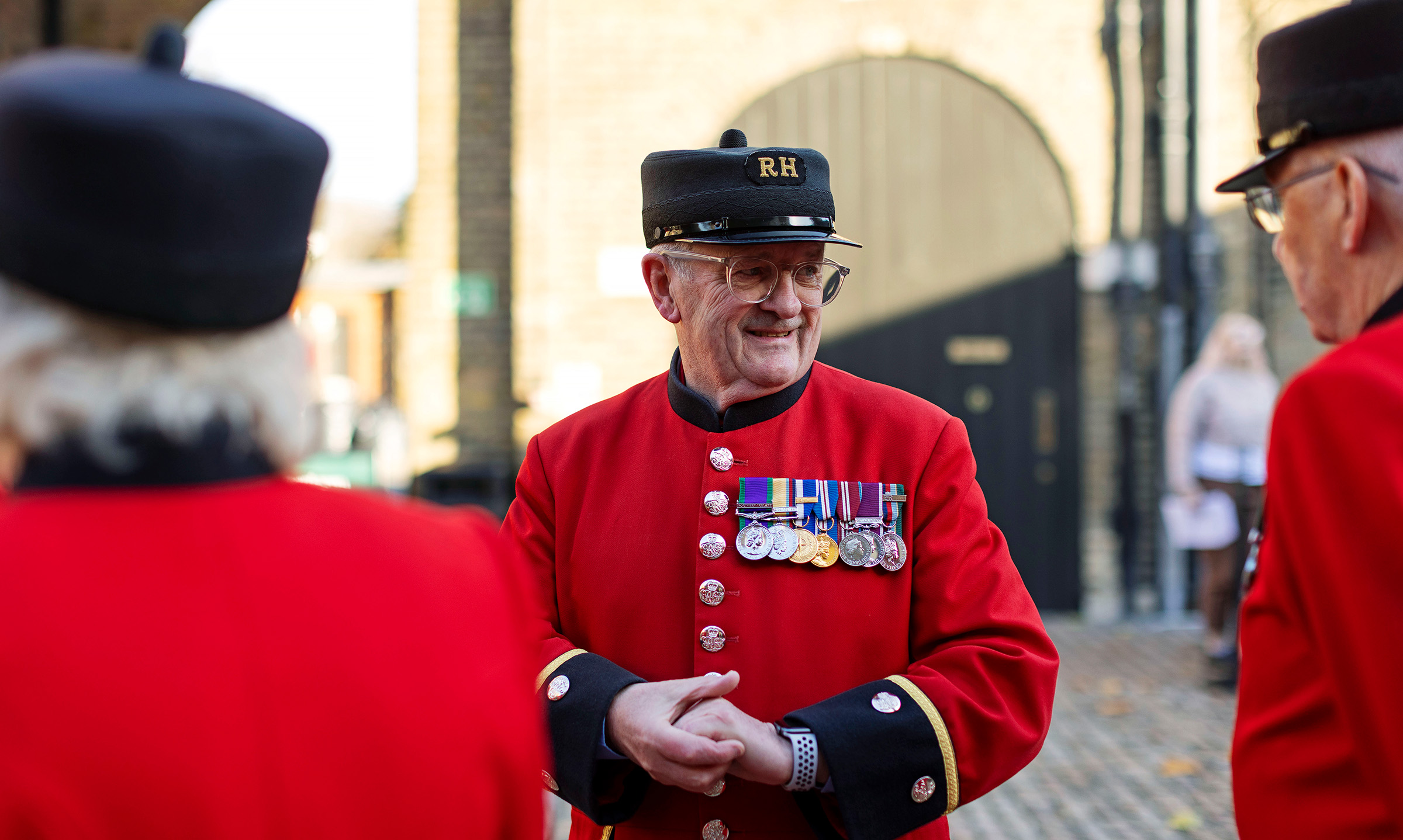 Chelsea Pensioner in a scarlet uniform with medals chatting with fellow residents in the Soane Stable Yard at the Royal Hospital Chelsea.