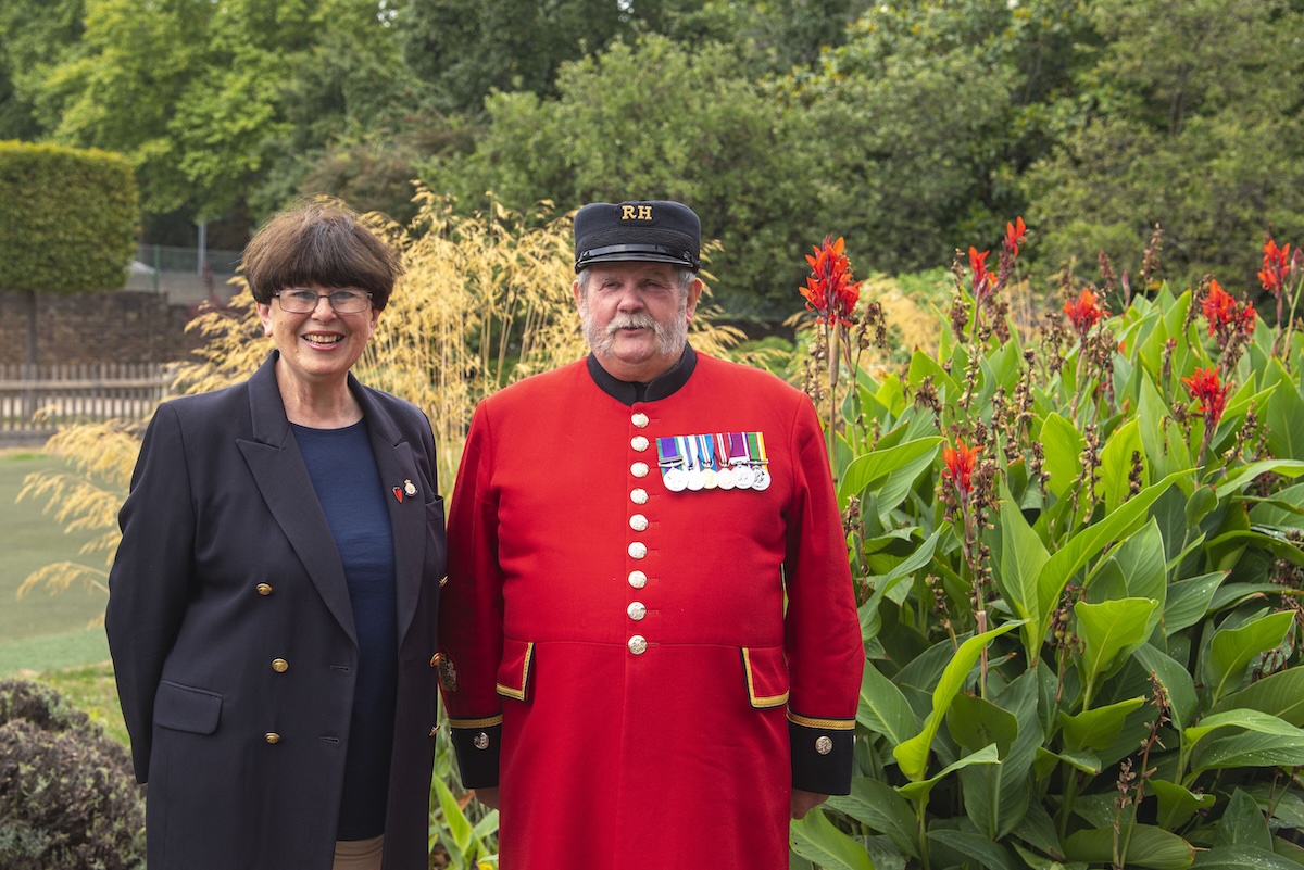 A supporter stands alongside a Chelsea Pensioner dressed in his iconic scarlet uniform in a lush green garden