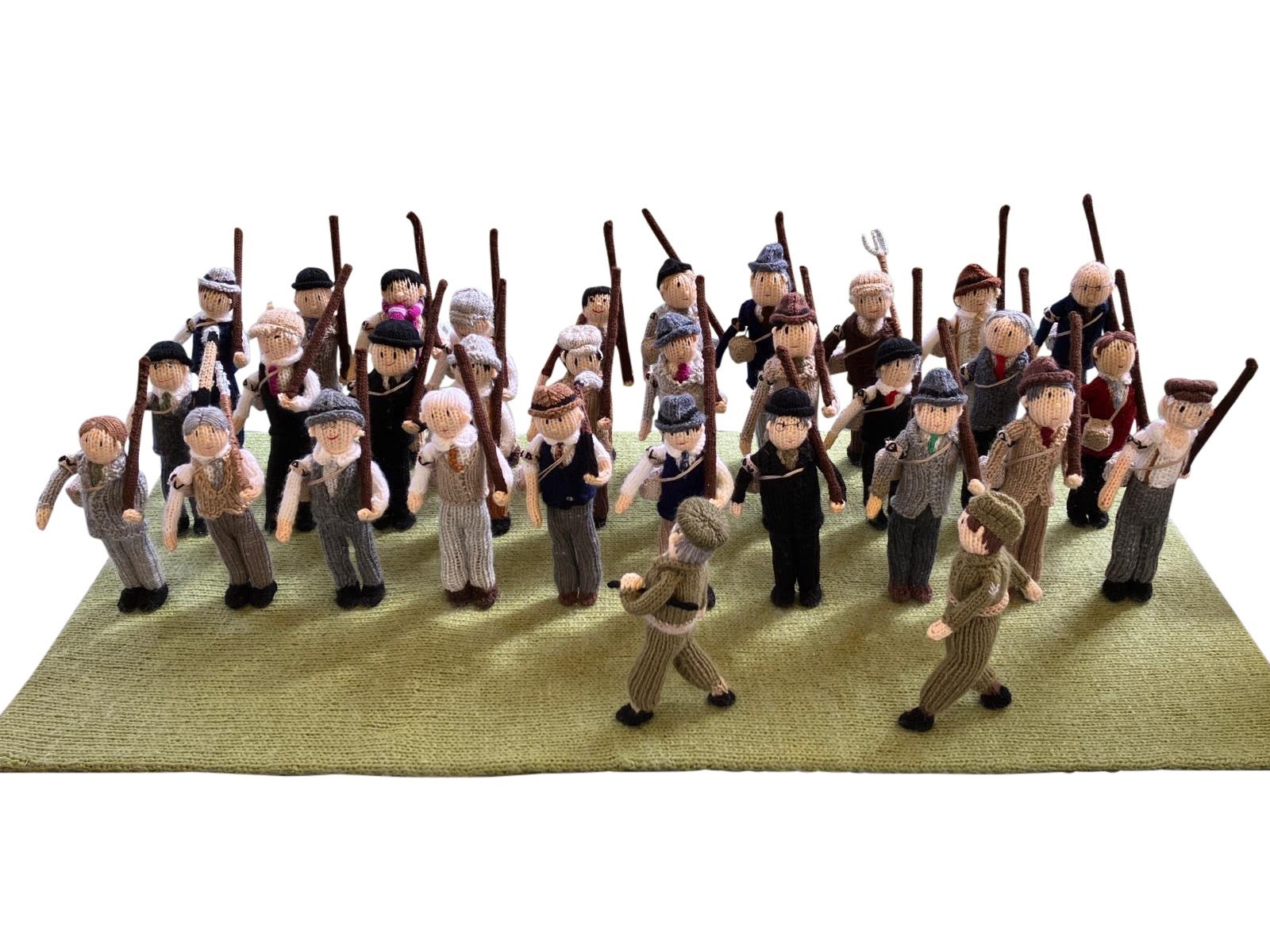 Crocheted diorama of a Home Guard platoon, civilian men in everyday dress standing in ranks with improvised pitchforks and sticks in place of rifles, part of The Longest Yarn WWII display.