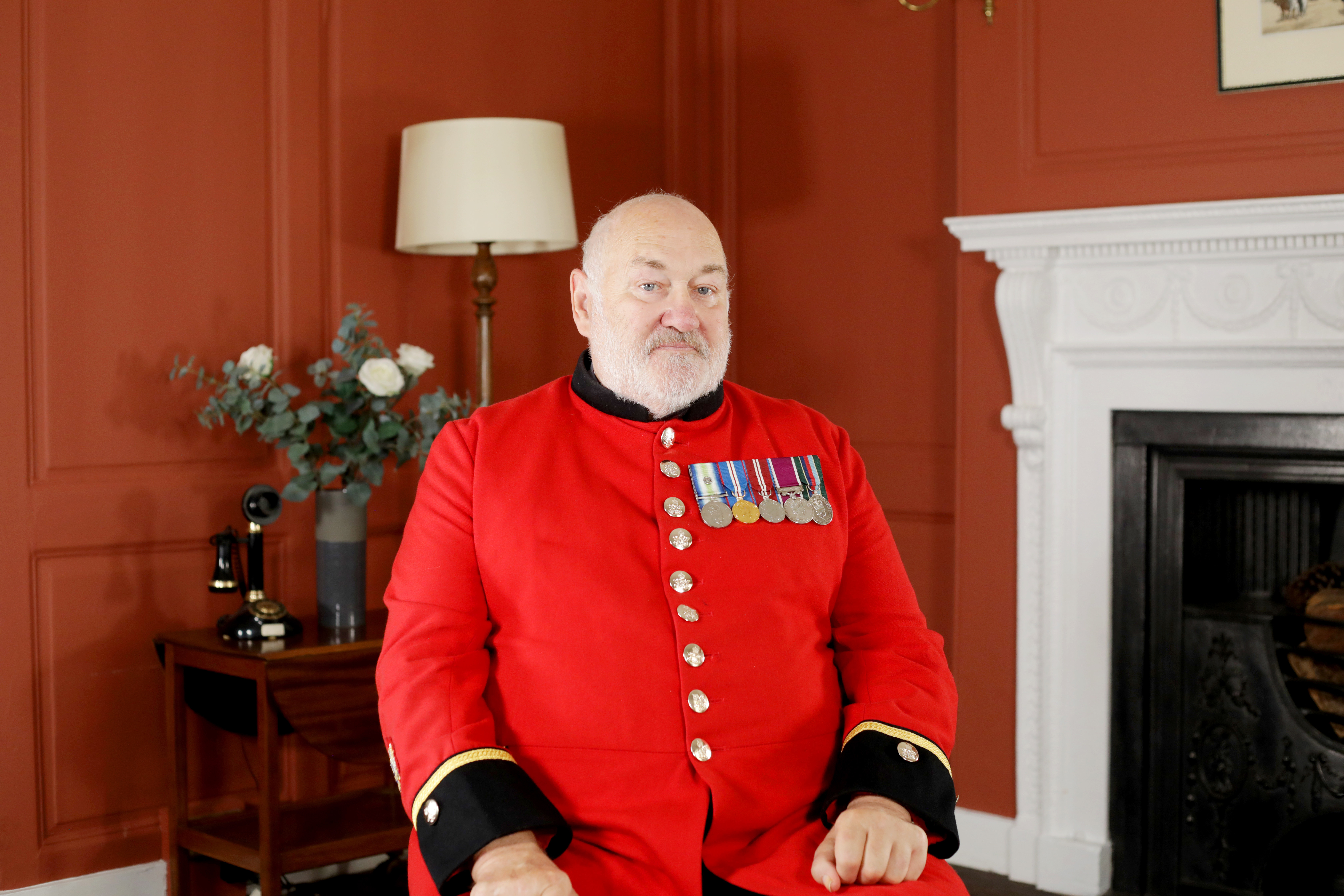 Chelsea Pensioner David Pratt sitting on a chair in his red scarlet uniform