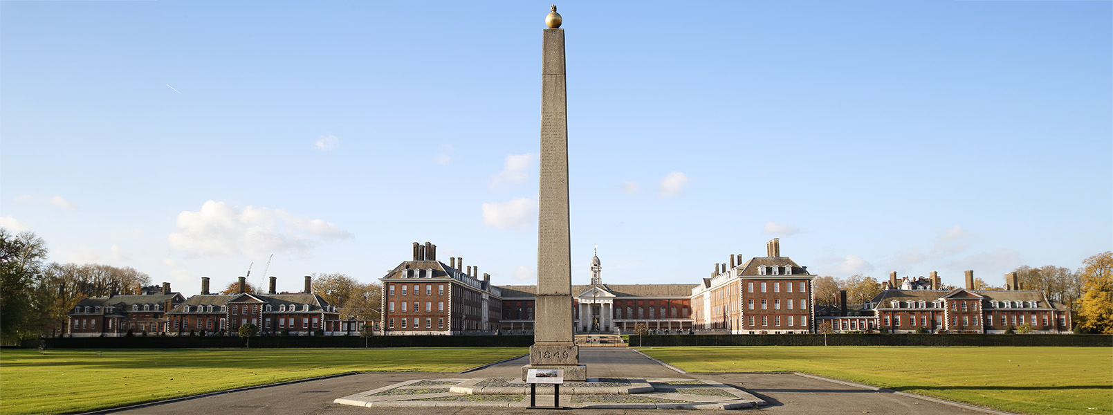 Chilianwala Obelisk Memorial situated in the grounds of the Royal Hospital Chelsea, set against a blue clear sky with the Royal Hospital buildings in the background.