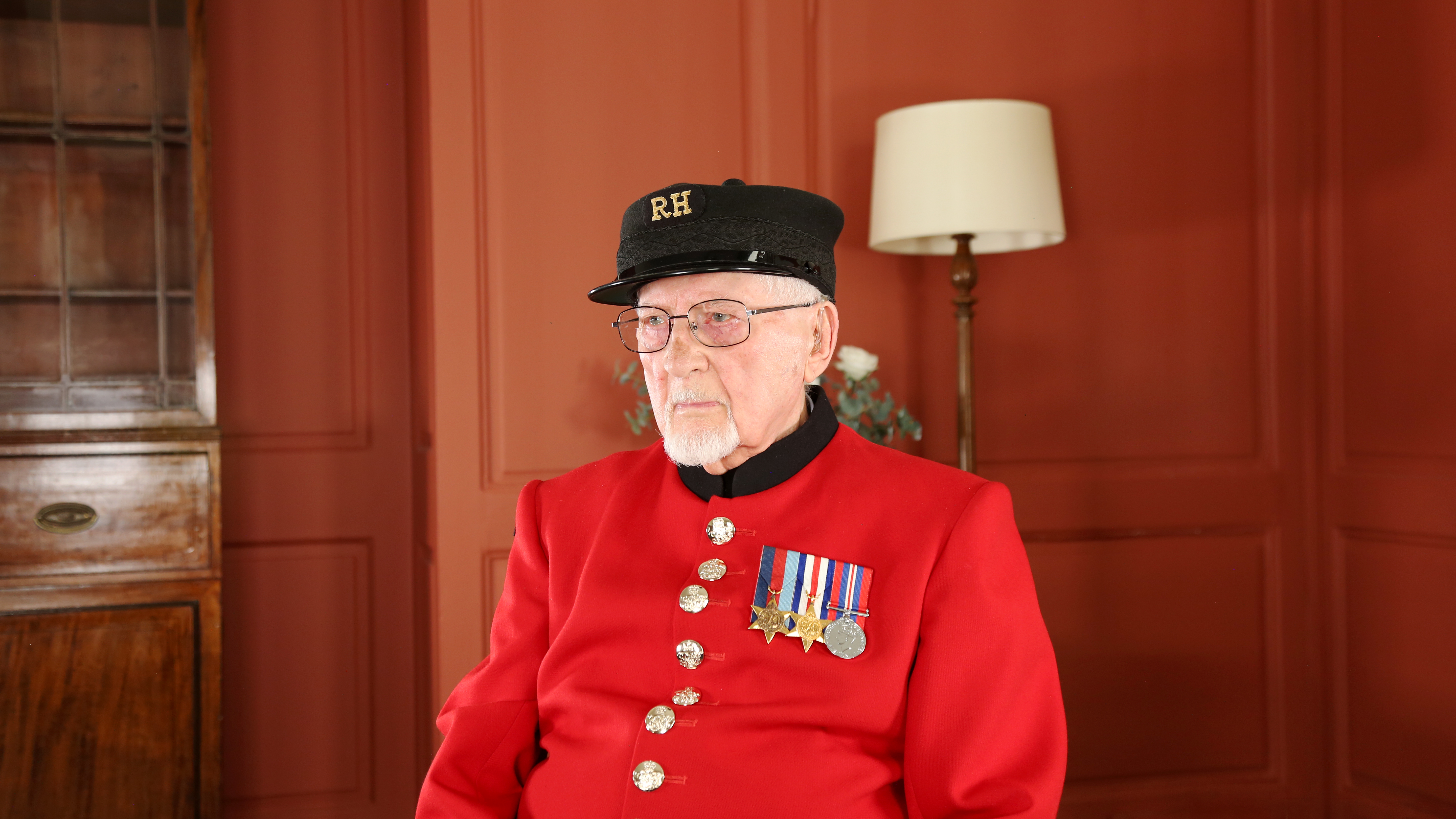 Chelsea Pensioner Brian sitting on a chair in his red scarlet uniform