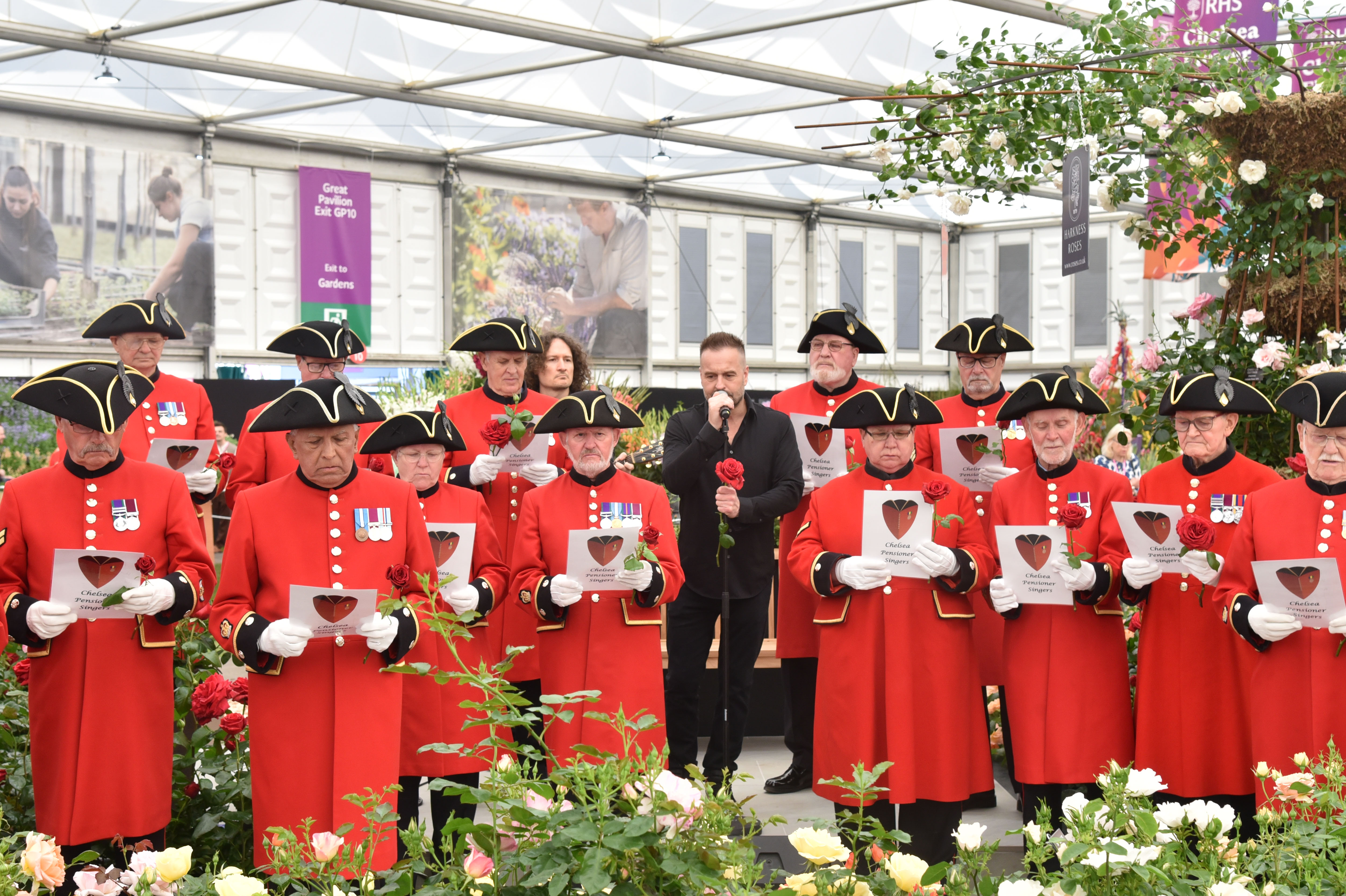 Chelsea pensioner singing group in scarlet coat and tricorne hat singing with Alfie Boe surrounded by red roses