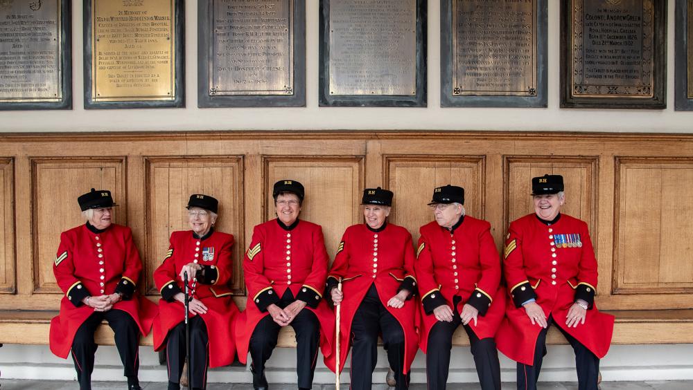 A group of female Chelsea Pensioners are sat laughing together on the colonnade at the Royal Hospital Chelsea