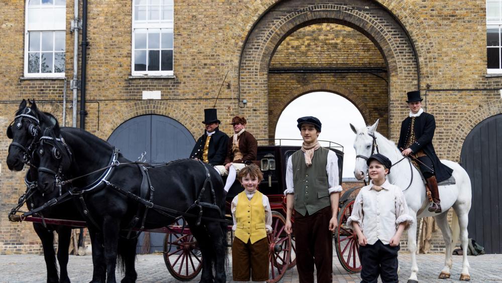 A group of costumed re-enactors stand together with a horse-drawn carriage at the newly renovated Soane Stable Yard