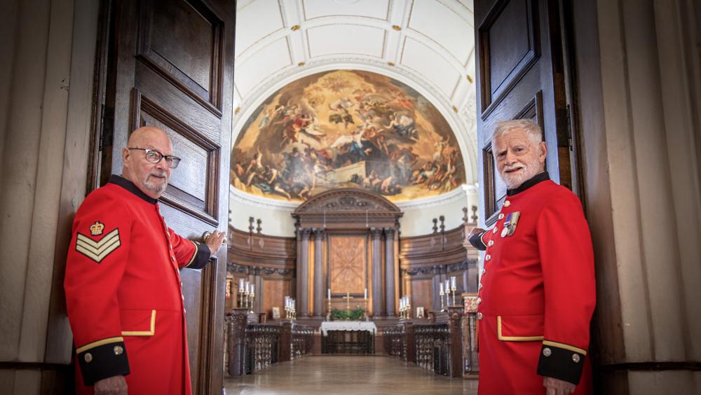 Two Chelsea Pensioners stand aside to welcome you as they open the doors of the Wren Chapel