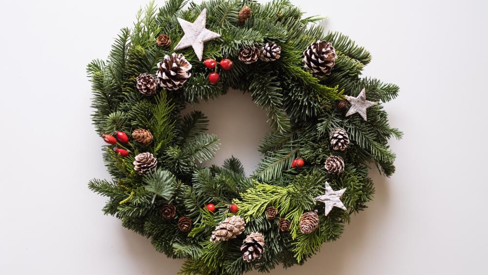 A green Christmas wreath decorated with silver stars, pine cones and red berries