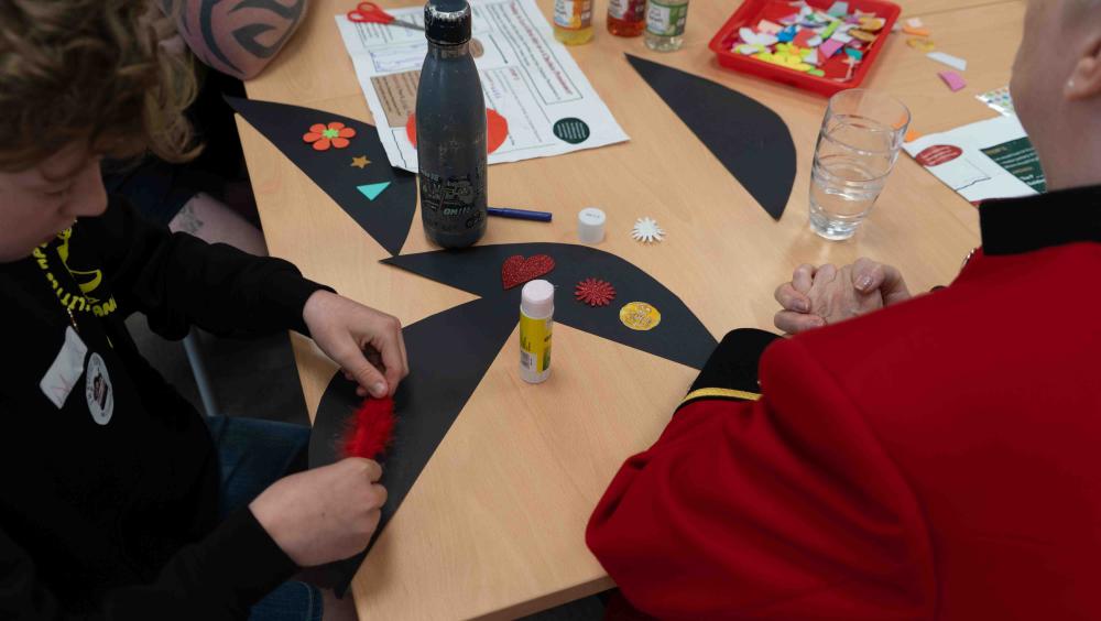A photo of an arts and crafts session featuring a Chelsea Pensioner and a participant. 