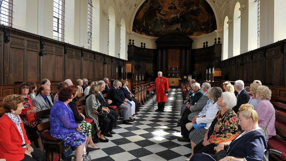 A scarlet-clad Chelsea Pensioner leads a tour of the public in the magnificent Wren Chapel