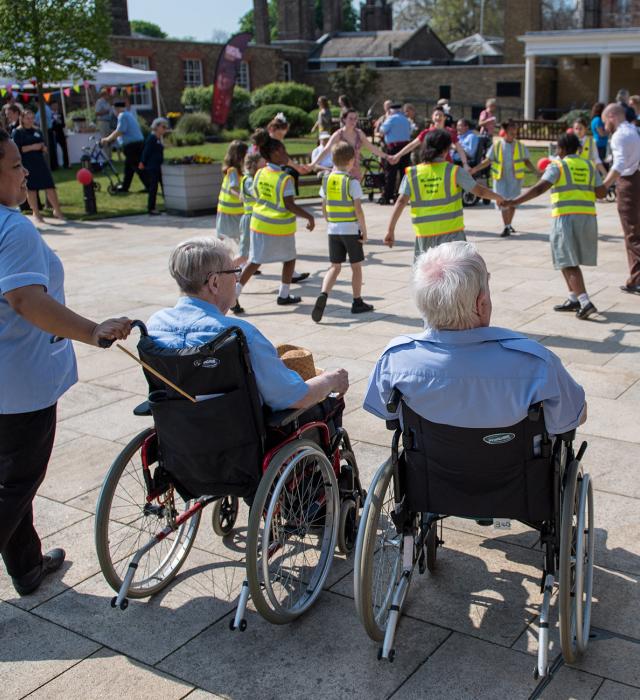 Carers pushing Chelsea Pensioners in wheelchairs at a lively outdoor event