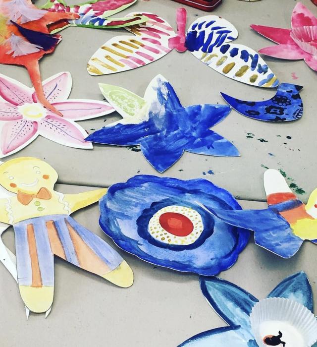 A variety of cut-out, hand-painted, paper shapes are sprawled across a grey table.