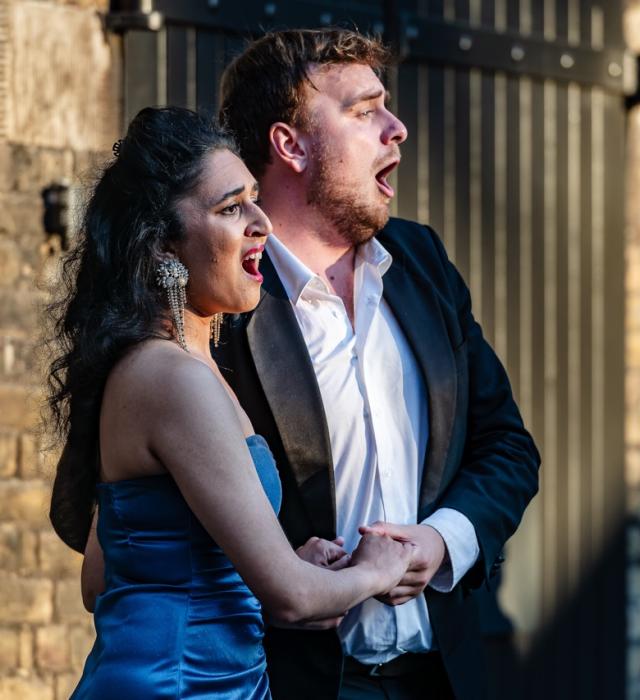 A well dressed male and female hold hands while singing in the Soane Stable Yard courtyard.