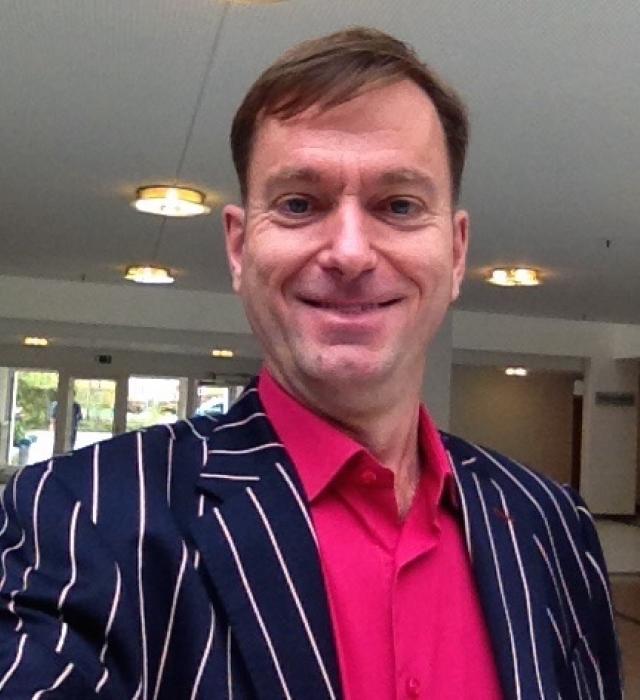 Edward Richards a British Sign Language Tour Guide - dressed in an immaculate blue suit jacket featuring white pinstripes and a striking pink shirt.