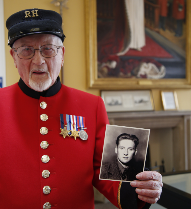 An image of Chelsea Pensioner Brian, a WWII veteran, holding up a photo of himself taken when he served