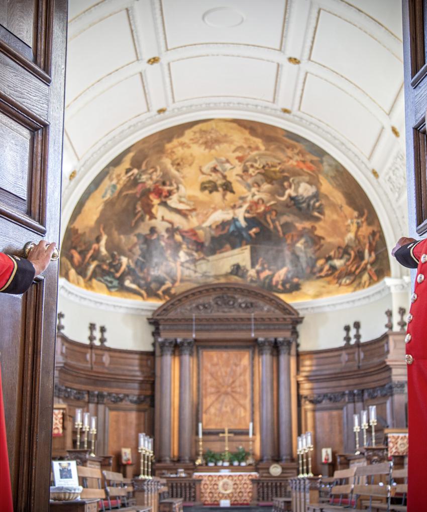 Two Chelsea Pensioners stand aside to welcome you as they open the doors of the Wren Chapel