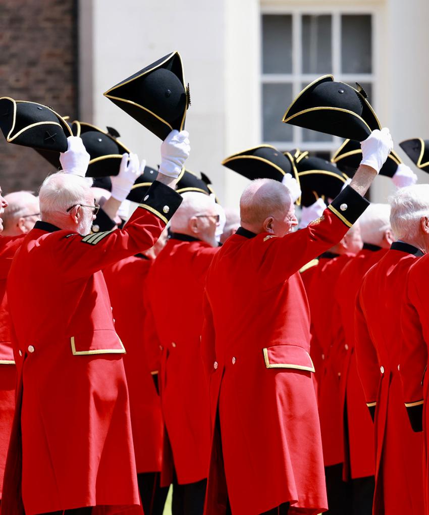 A group of Chelsea Pensioners standing with their Tricorne hats lifted off their head in salute during Founders Day 2024