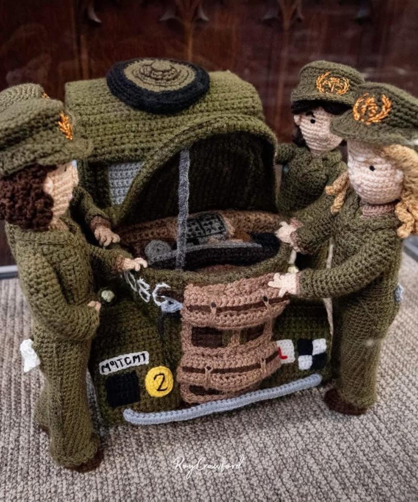 Crocheted military diorama of three uniformed soldiers working on an open-bonnet army truck, part of The Longest Yarn WWII display.