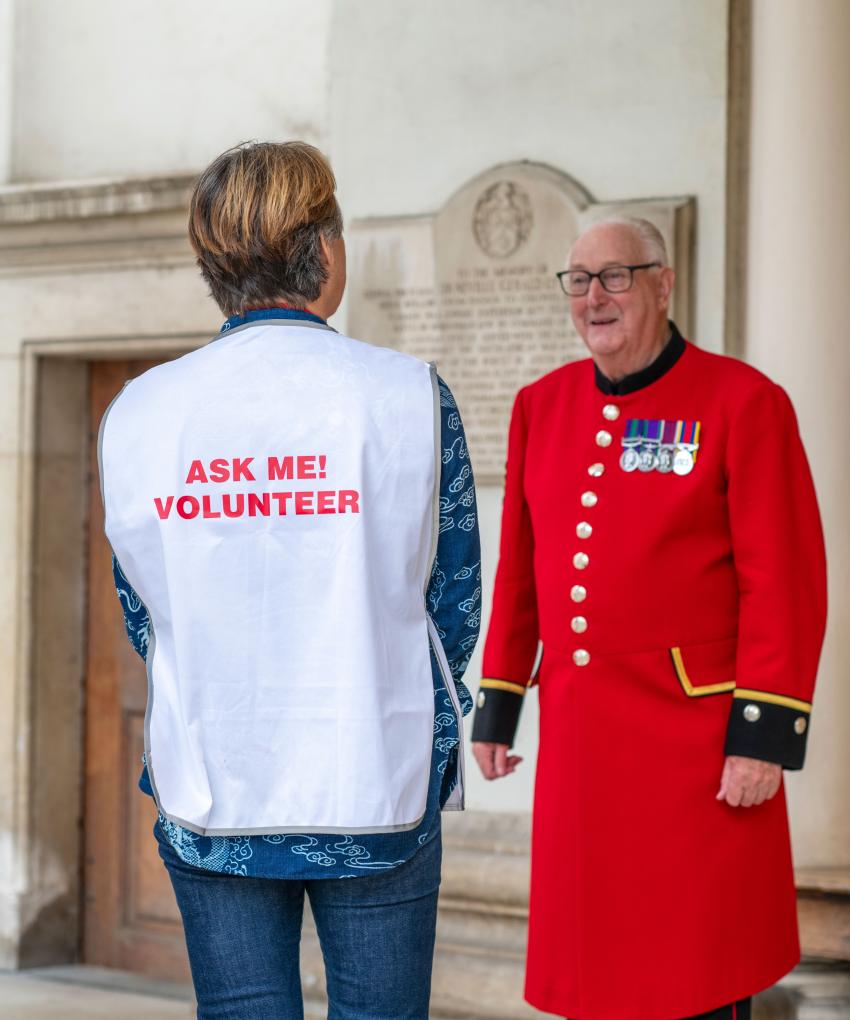 An image of a volunteer whos back is facing the camera, having a conversation with a Chelsea Pensioner at Royal Hospital Chelsea