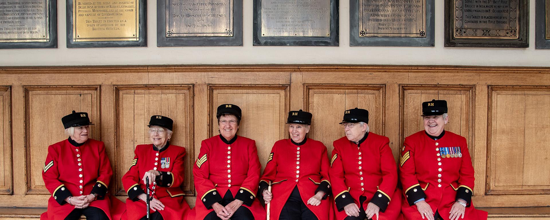 A group of female Chelsea Pensioners are sat laughing together on the colonnade at the Royal Hospital Chelsea