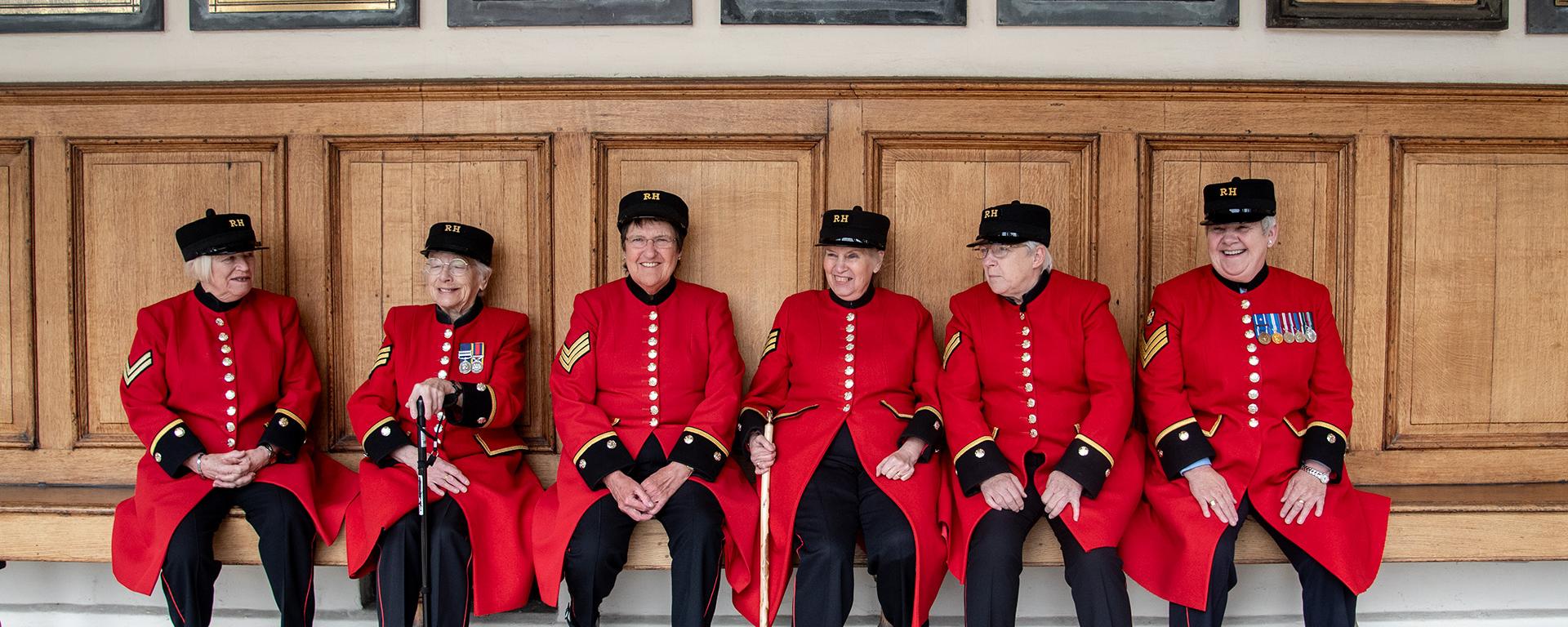 A group of female Chelsea Pensioners are sat laughing together on the colonnade at the Royal Hospital Chelsea