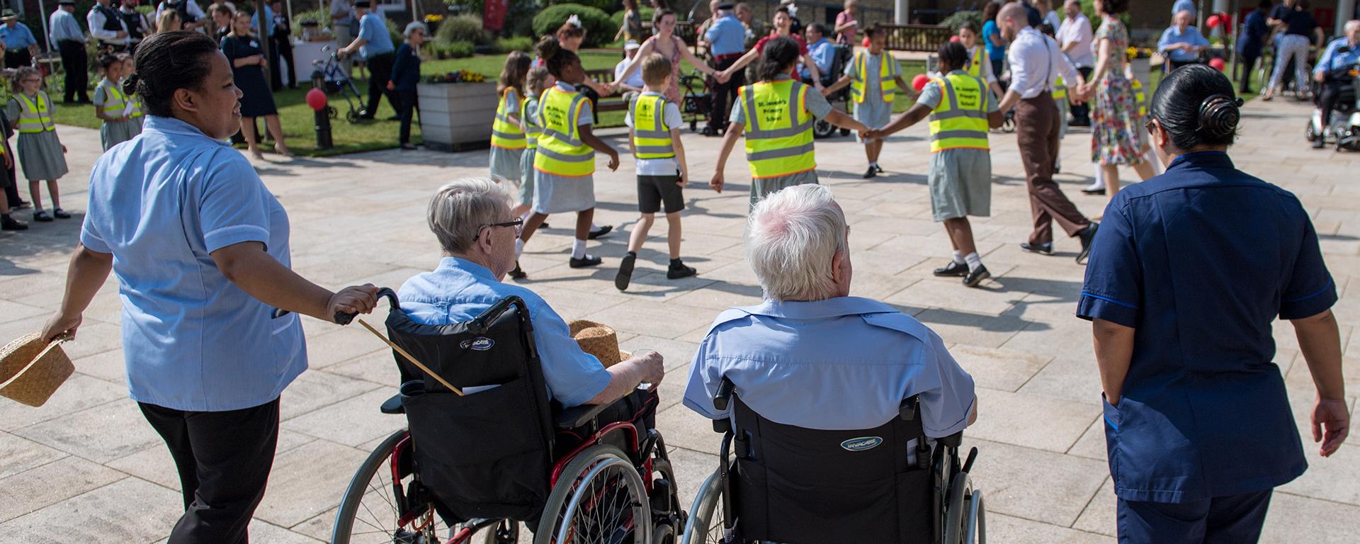 Carers pushing Chelsea Pensioners in wheelchairs at a lively outdoor event