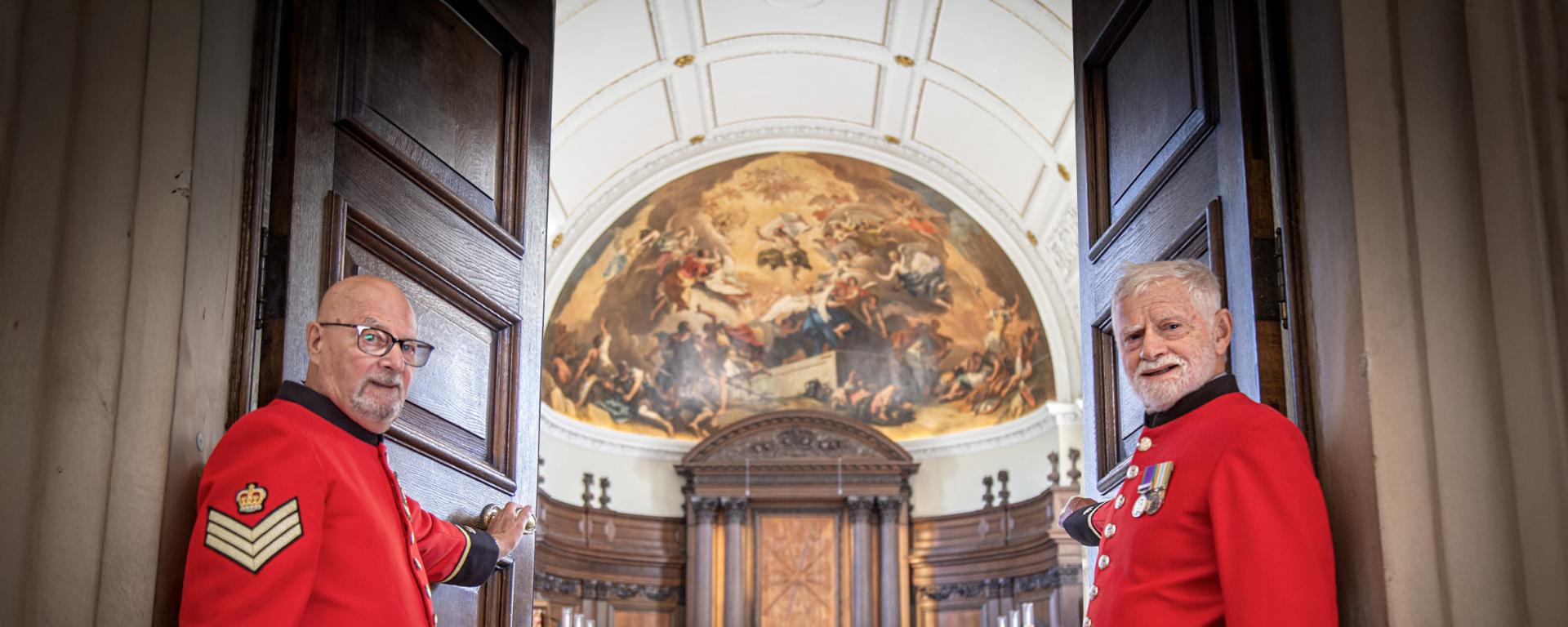 Two Chelsea Pensioners stand aside to welcome you as they open the doors of the Wren Chapel