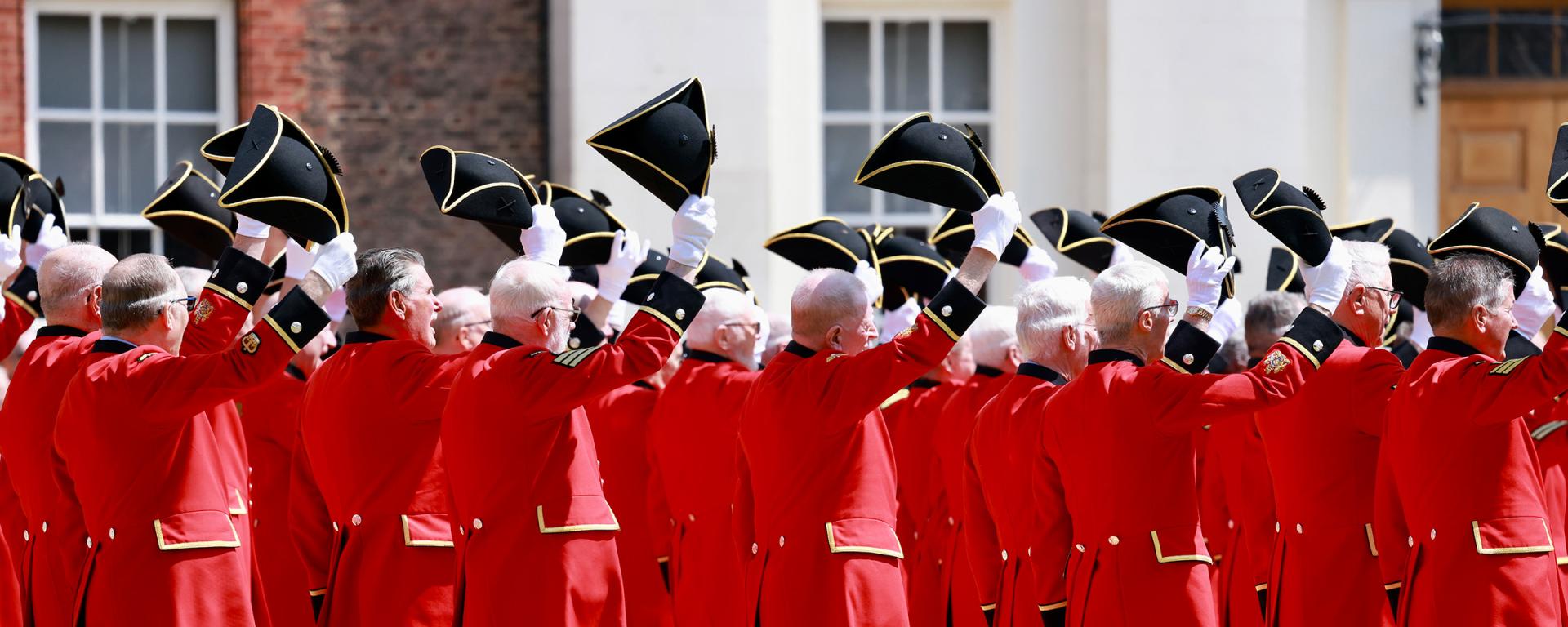 A group of Chelsea Pensioners standing with their Tricorne hats lifted off their head in salute during Founders Day 2024