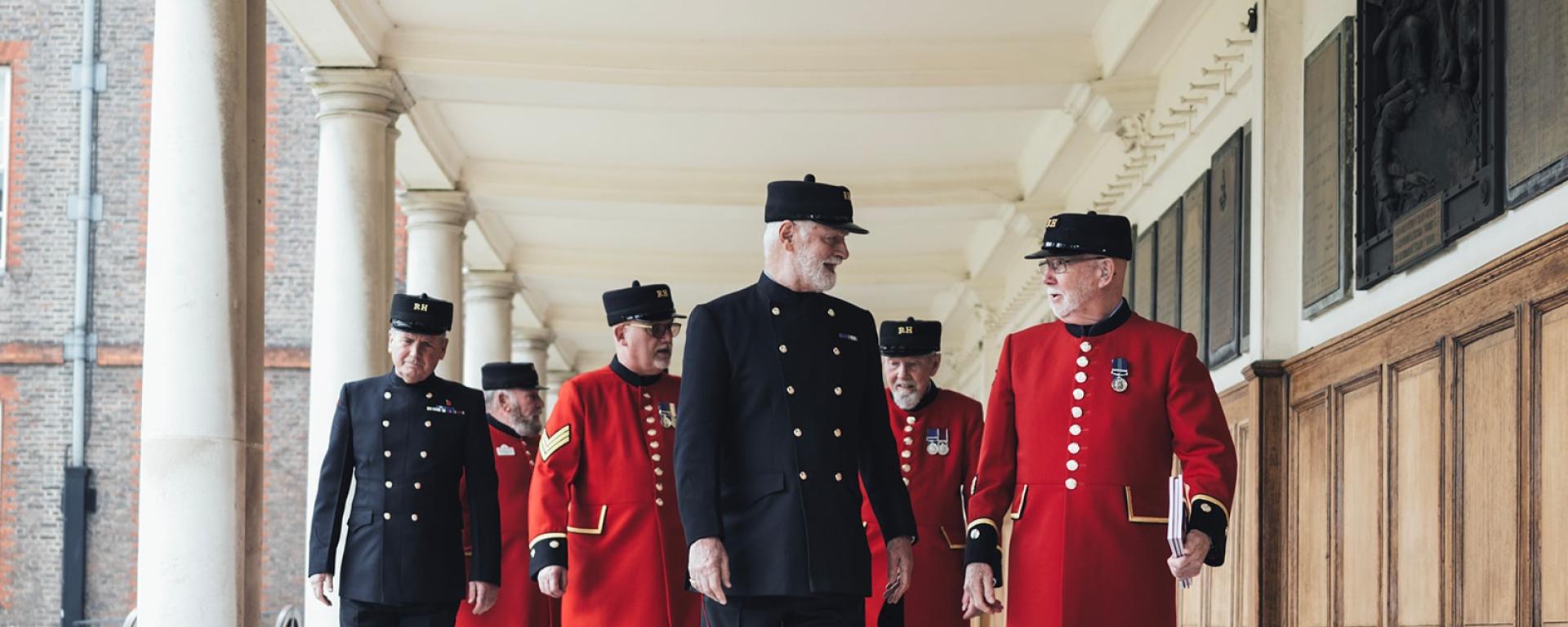 A photo of a group of Chelsea Pensioners walking towards the camera along the Figure Court colonnade. 