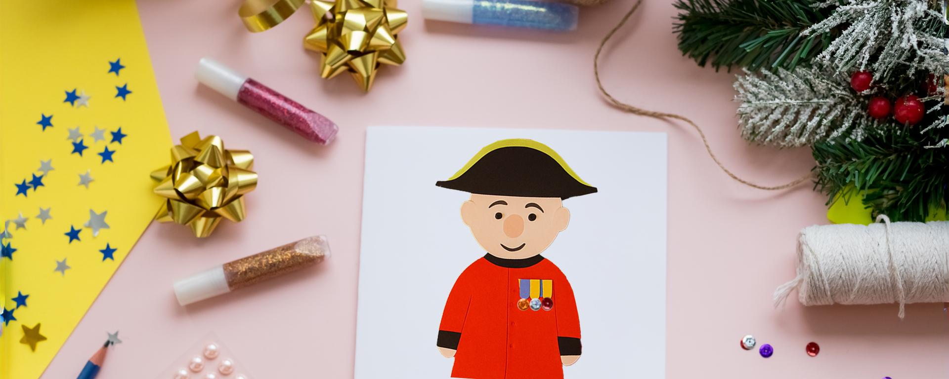 A colourful table adorned with craft making suppliers a Christmas Garlands. A Christmas card depicts a hand crafted Chelsea Pensioner