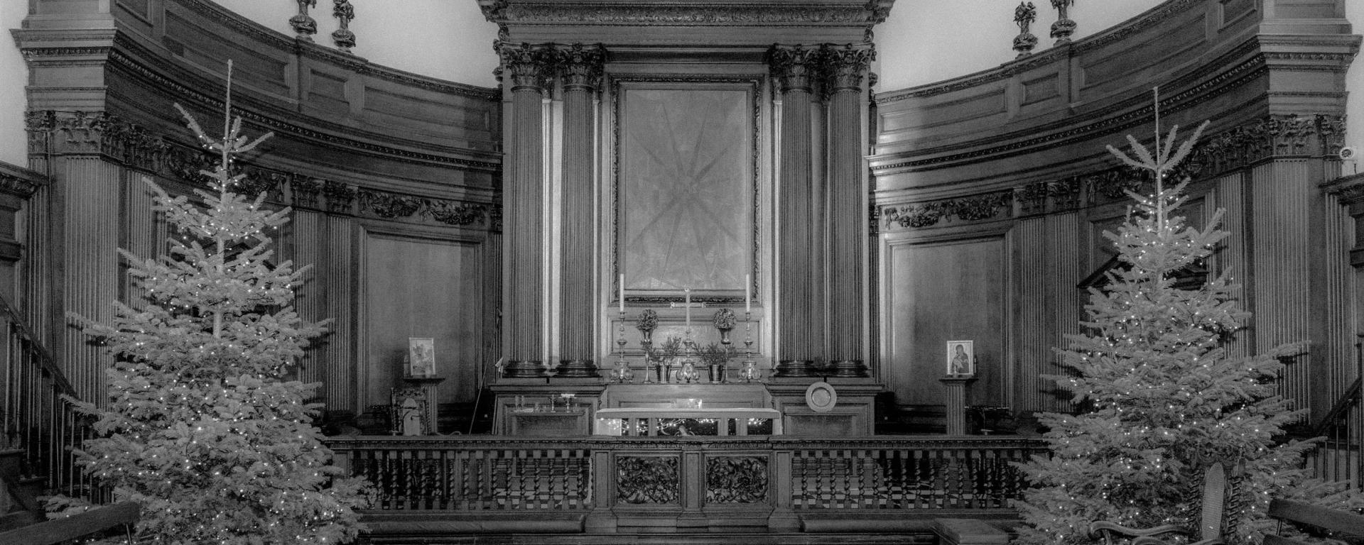 An old black and white photo of the alter at the Royal Hospital Chelsea's Wren Chapel - with Christmas trees on either side of the photo
