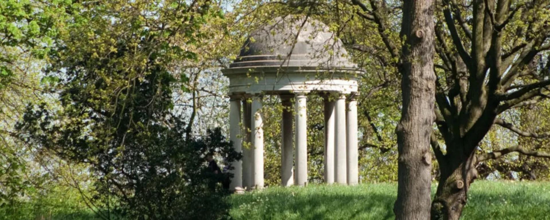 The Temple of Aeolus, a circular classical pavilion, set among trees and greenery in the grounds of Kew Gardens