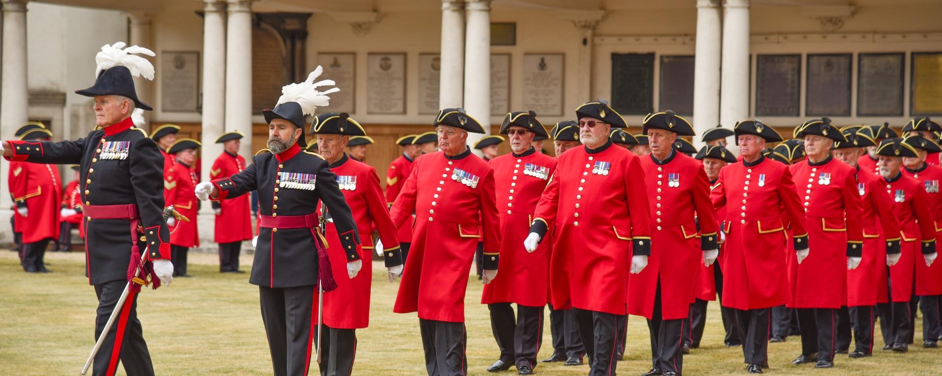 Chelsea Pensioners dressed in Scarlet uniform, alongside military staff in ceremonial uniform, march on figure court at The Royal Hospital Chelsea