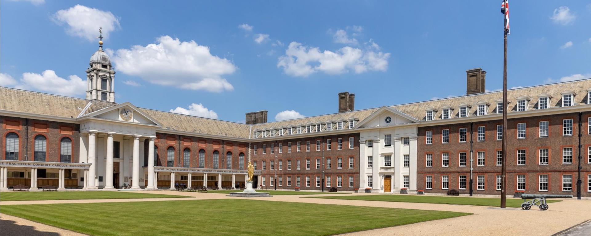 Panoramic view of Figure Court at the Royal Hospital Chelsea, showing the Wren Chapel, historic red brick buildings, statue of King Charles II and the central parade ground.