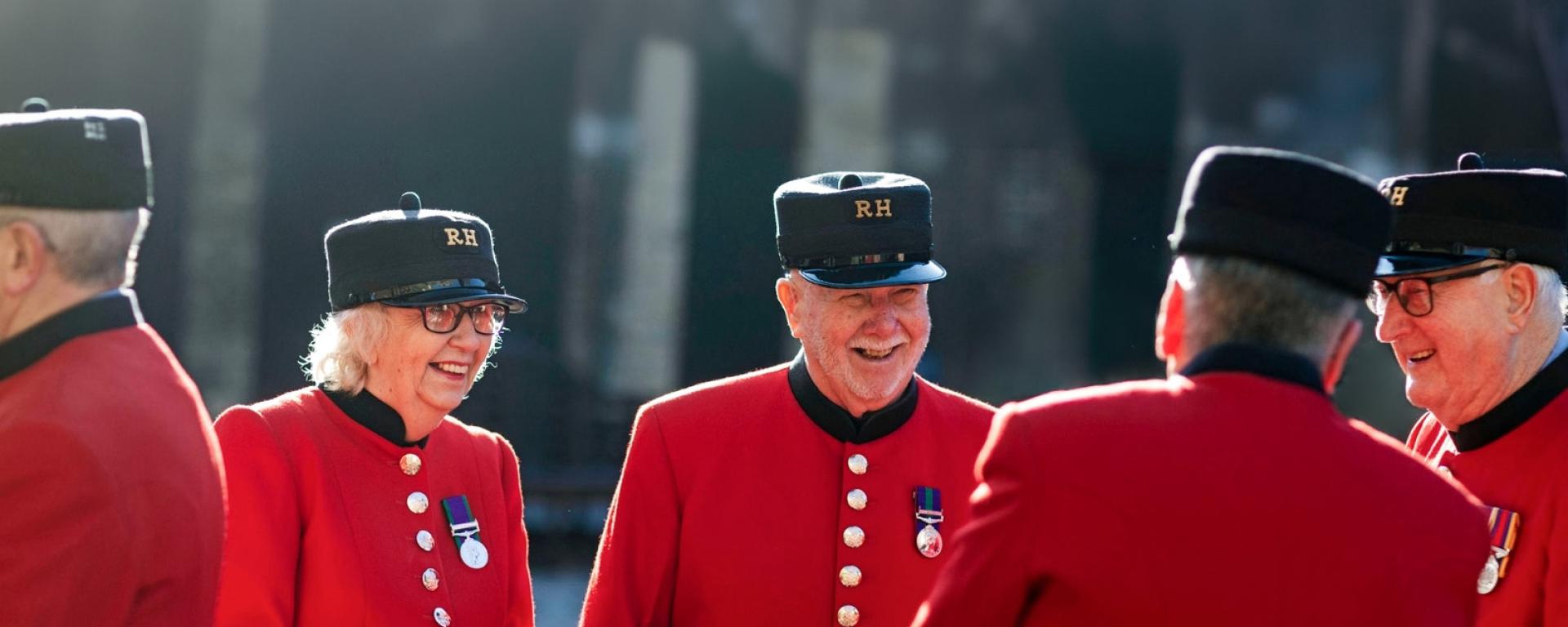 A group of Chelsea Pensioners dressed in their iconic scarlet uniform, laugh and joke in an outside courtyard