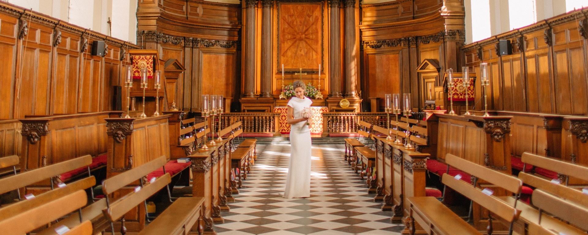 Bride standing in the aisle of the Chapel at the Royal Hospital Chelsea, surrounded by historic wood panelling and traditional furnishings.