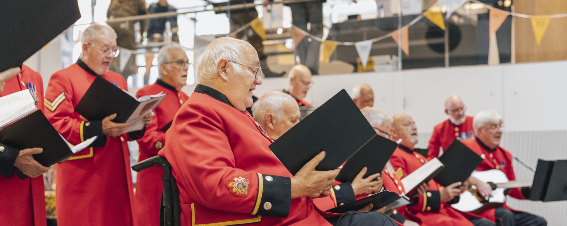 An image of the Chelsea Pensioners in their iconic scarlet uniforms singing as part of a Chelsea History Festival event at Royal Hospital Chelsea 