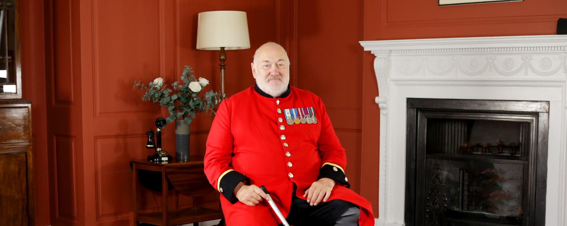 Chelsea Pensioner David Pratt sitting on a chair in his red scarlet uniform